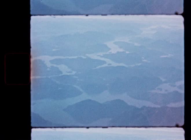 Vintage film captures a hazy, blue-toned aerial view of a vast archipelago or fjord system