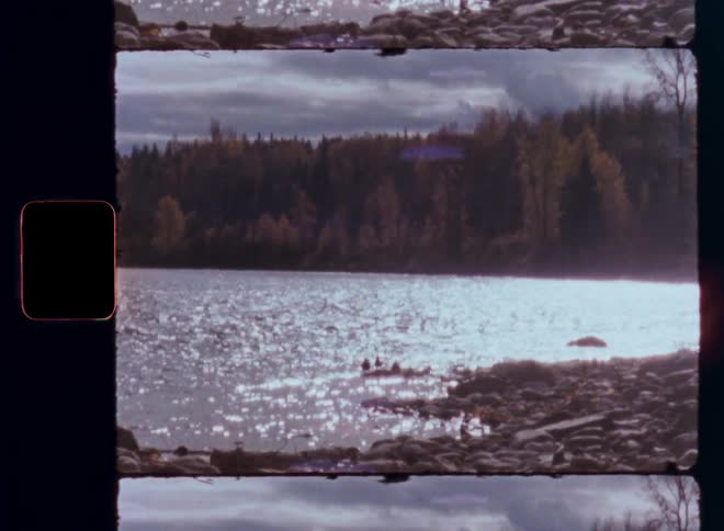 Sunlight glitters on a serene lake surrounded by a dense forest in this vintage 8mm film footage