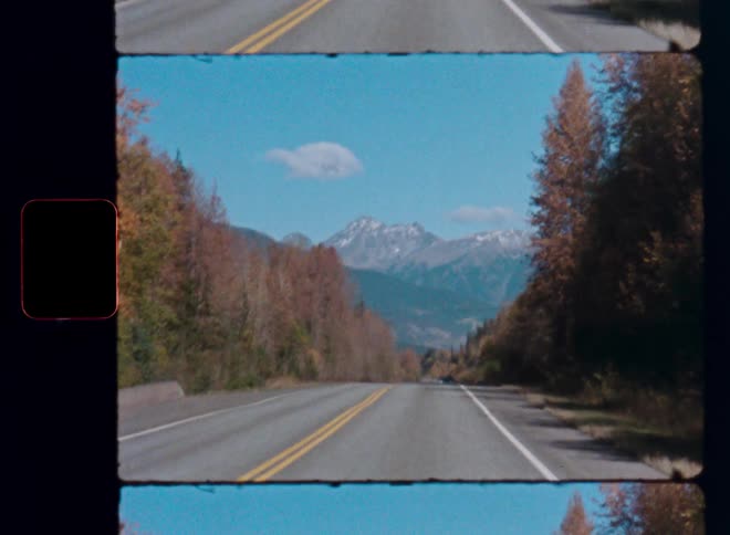 Vintage film view from a car driving on an empty highway towards majestic snow-capped mountains in the autumn