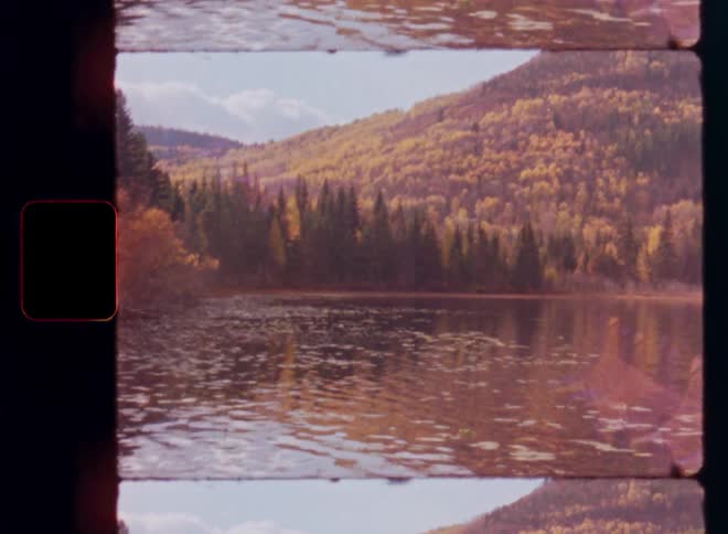 Authentic vintage film shows a tranquil lake reflecting the golden autumn trees on a mountainside