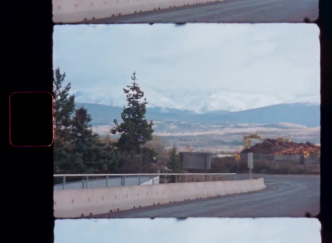 A vintage 8mm film captures the view of a winding road leading towards majestic snow-capped mountains