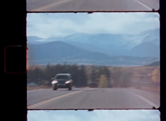 Vintage film captures a first-person view driving towards majestic snow-capped mountains as another car passes