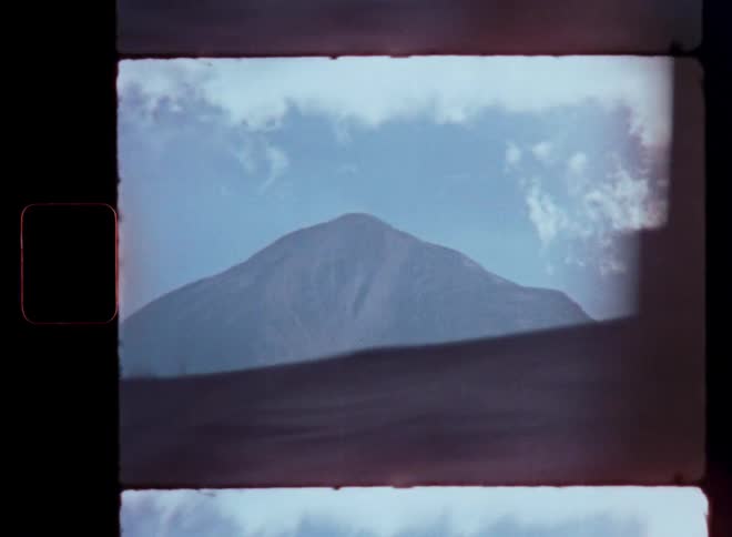 A view from a moving vehicle reveals a hazy mountain peak with trees and power lines in the foreground, shot on vintage film