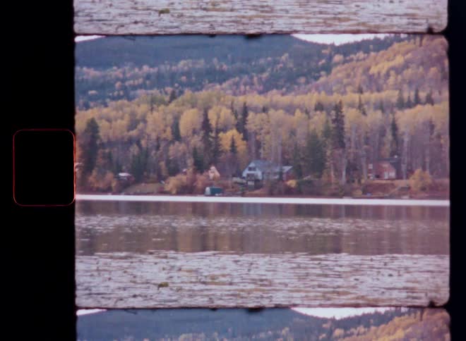 Vintage film captures a tranquil lake with cabins nestled among colorful autumn trees on the distant shore