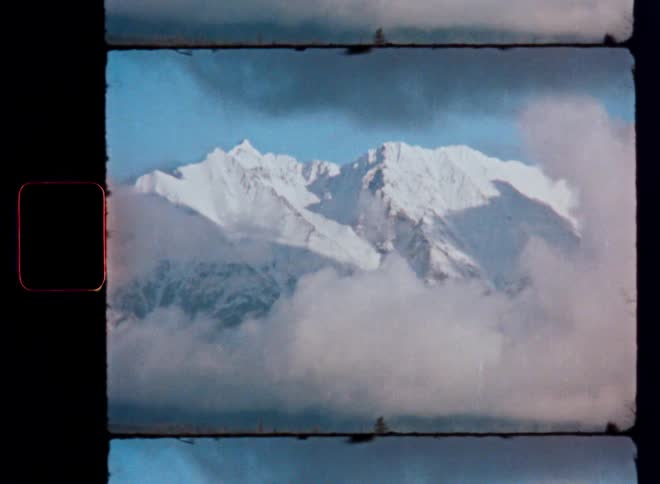 Archival film footage shows majestic snow-capped mountains rising above a bed of clouds and a forest