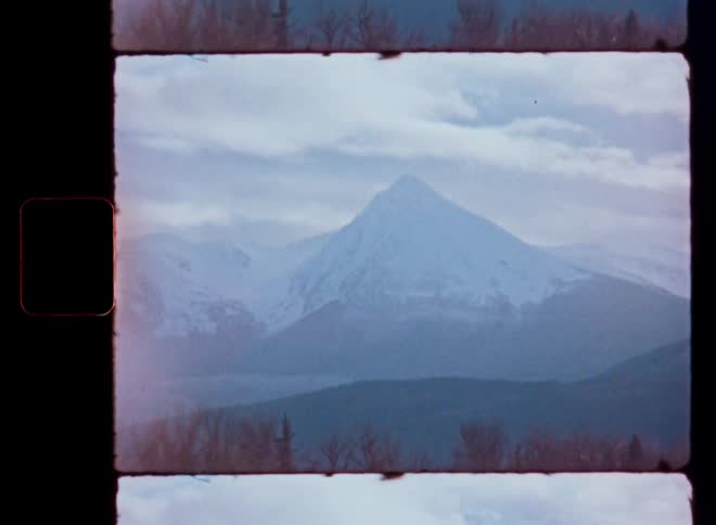 Archival Super 8mm film footage captures a beautiful, snow-covered mountain peak on an overcast day