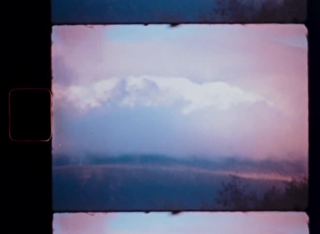 Dreamy vintage 8mm footage shows foggy clouds slowly clearing to reveal a snow-capped mountain range