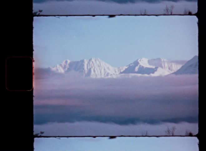 A dreamy vintage shot shows a majestic snow-covered mountain range rising above a sea of clouds