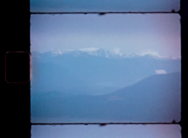 Vintage 8mm film captures a static, hazy view of a distant, snow-capped mountain range