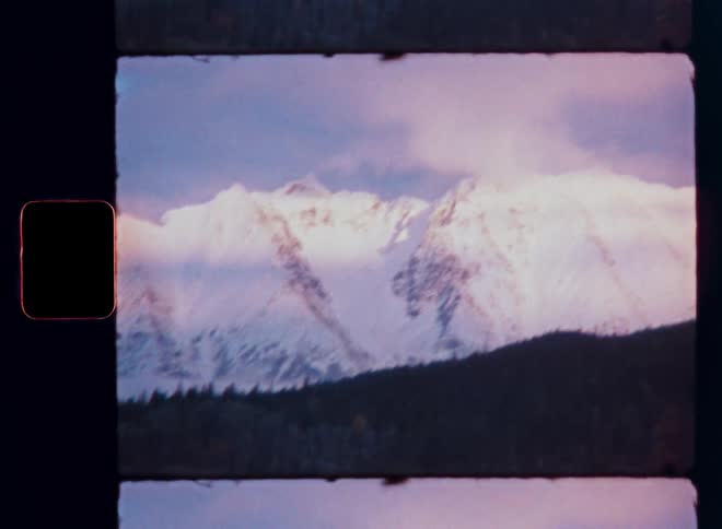 Super 8 film scan of majestic, snow-covered mountain peaks bathed in the pink light of sunrise