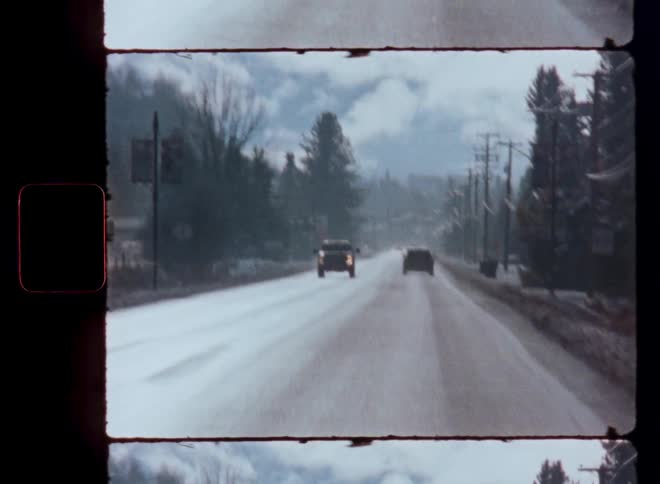 Vintage film footage captures a drive down a snowy road in a small town during winter