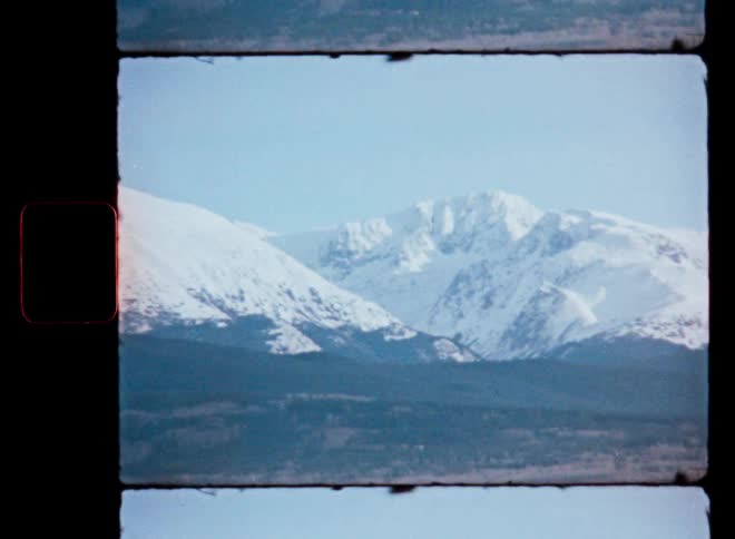 An authentic Super 8mm film scan captures a static wide shot of a majestic snow-covered mountain range on a clear day