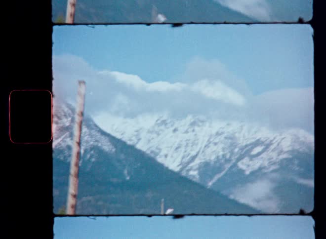 Driving past snow-covered mountains on a sunny day, captured on grainy, vintage 8mm film