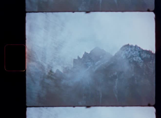 Vintage 8mm film captures a blurry drive-by view of a snow-capped mountain range shrouded in mist