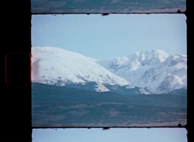 A vintage film shot slowly pans across a vast, snow-covered mountain range under a clear sky