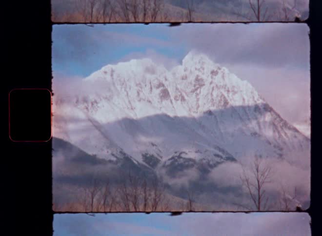 An 8mm film scan reveals a majestic, snow-covered mountain peak with trees in the foreground