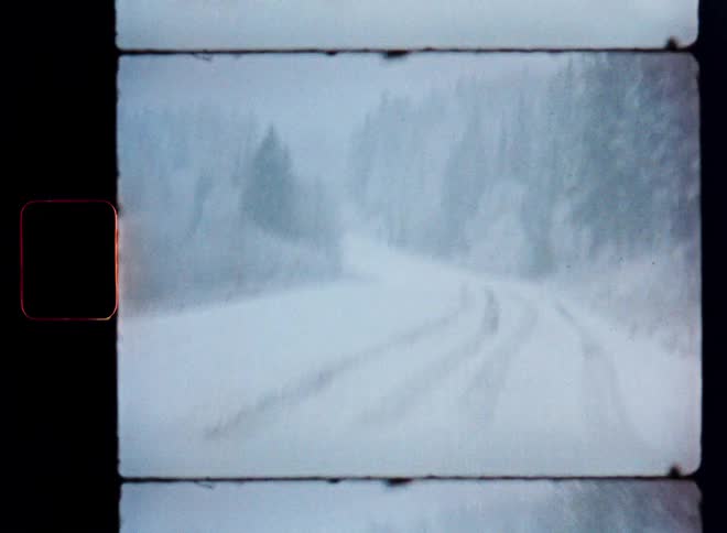 Authentic vintage film captures a desolate snow-covered road winding through a forest during a blizzard