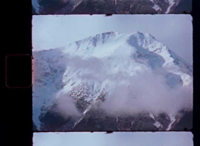 A vintage 8mm film captures a majestic snow-capped mountain as clouds slowly drift past its peak