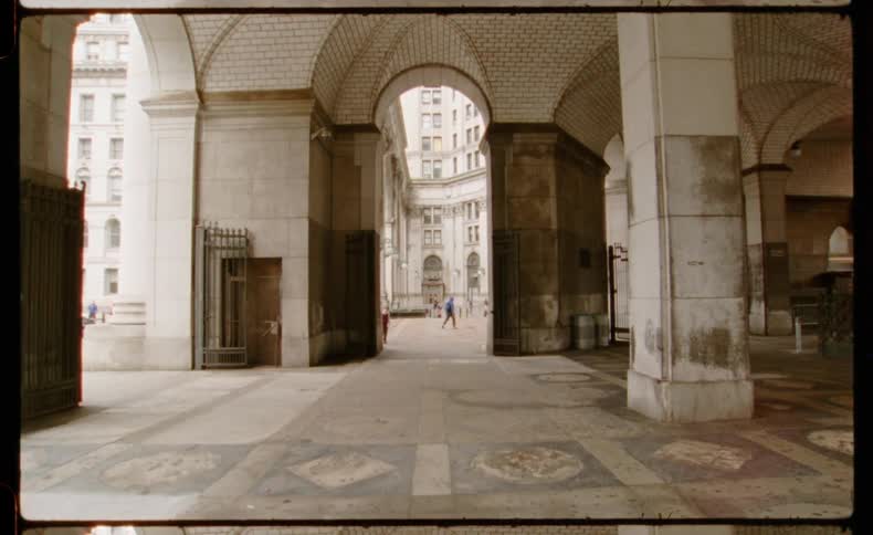 A vintage film-style view from under the grand arches of the Manhattan Municipal Building as people walk through the courtyard