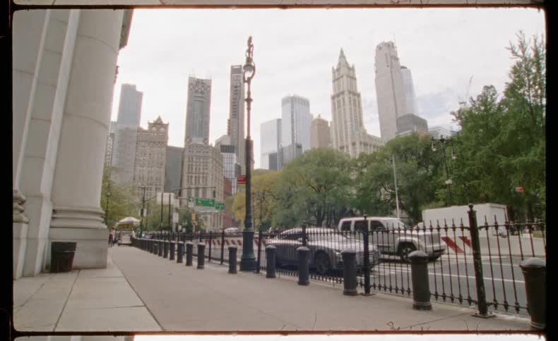 A vintage film-style shot of the New York City skyline with traffic passing by and a man walking on the sidewalk