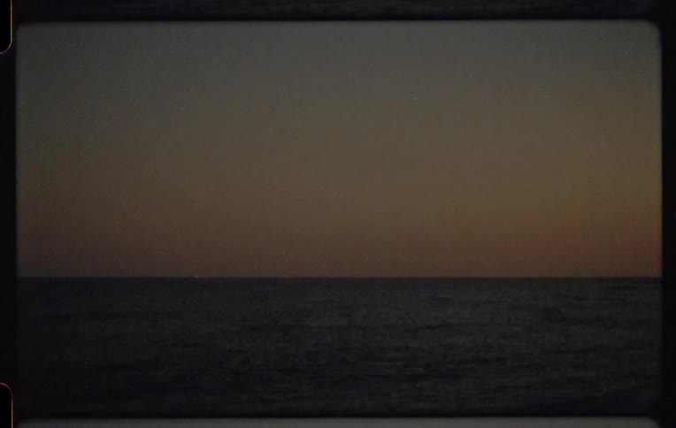 Vintage 8mm film captures a tranquil ocean scene at dusk with a warm glow on the horizon