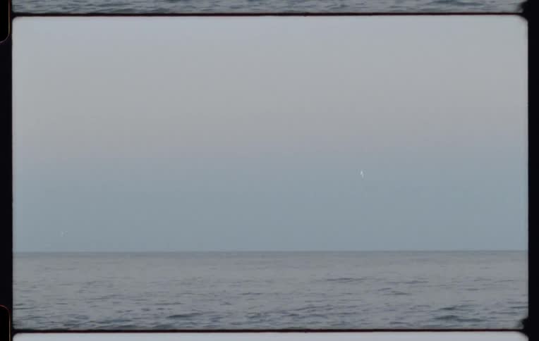 Calm ocean waves meet a hazy sky at the horizon in a vintage 8mm film shot