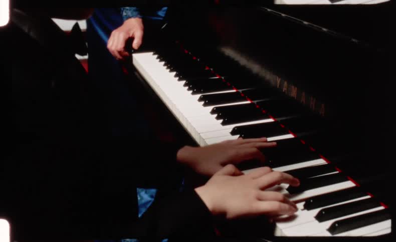 A close-up of a child's hands learning to play the piano with an adult guiding them, captured on vintage-style film