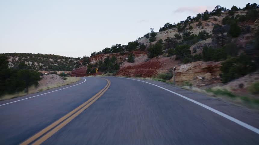 A serene point-of-view drive along a winding, empty road through a rocky desert canyon landscape at dusk