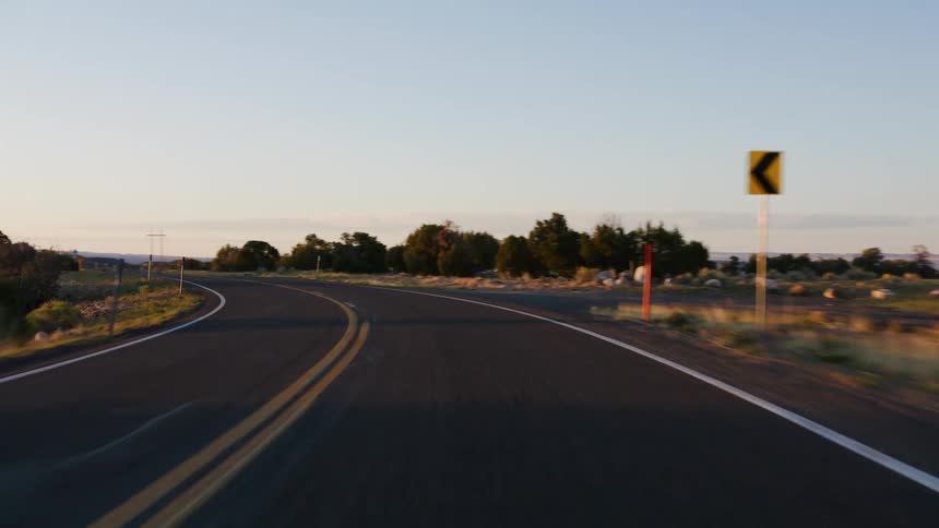 A smooth point-of-view shot driving down a winding desert road at sunrise