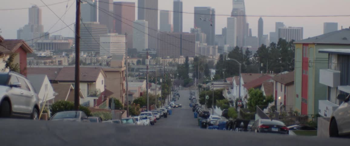 A slow zoom-out from a hilly residential street revealing the hazy Los Angeles skyline at dusk
