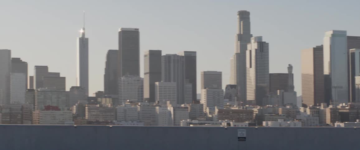 A slow panning shot of the Los Angeles downtown skyline on a hazy sunny day with a wall in the foreground