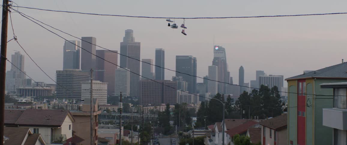 A slow zoom on the downtown Los Angeles skyline with shoes hanging from a power line in a residential neighborhood