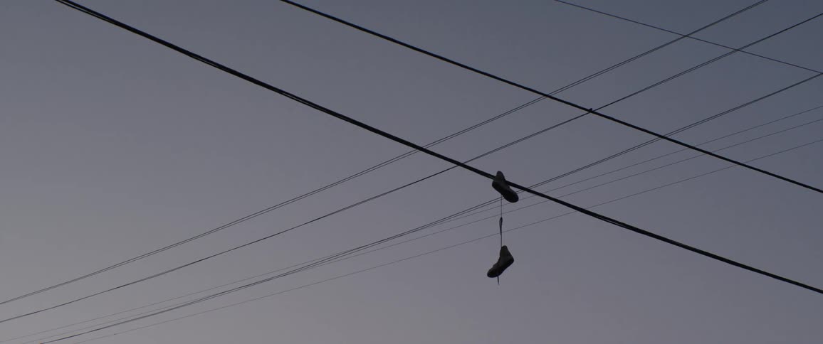 A pair of shoes dangles from a power line against a solid grey sky