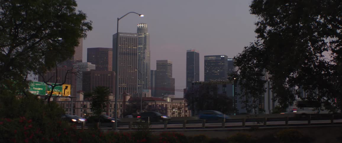 Cars drive along the freeway in front of the illuminated downtown Los Angeles skyline at twilight