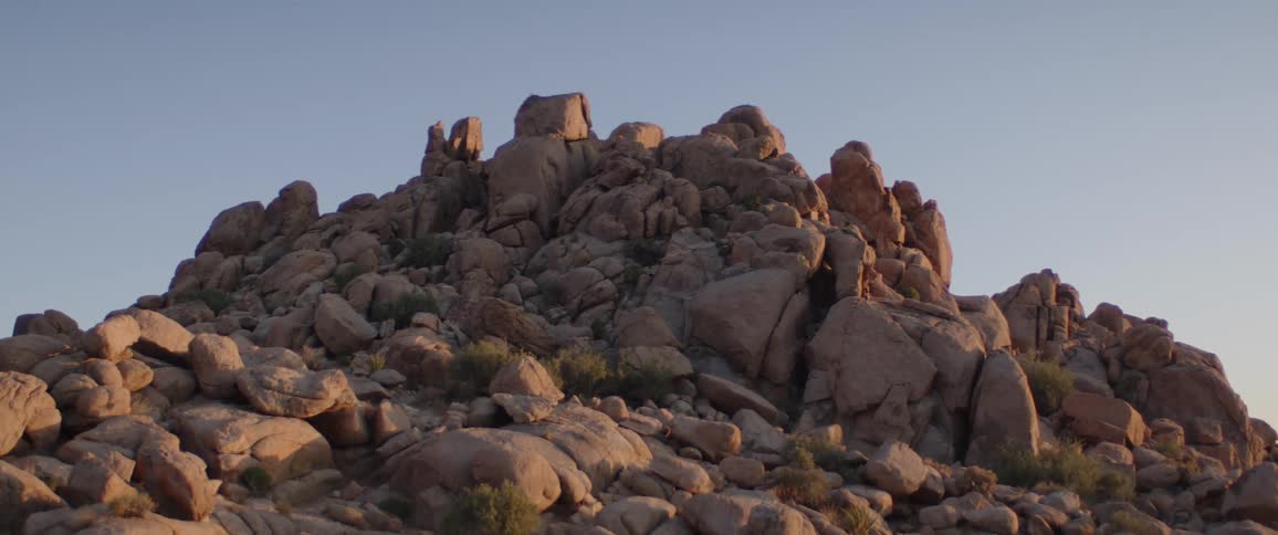 Golden hour light shines on a rocky desert mountain against a clear blue sky