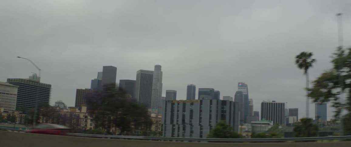 A moody drive-by view of the Downtown Los Angeles skyline on an overcast day from the freeway