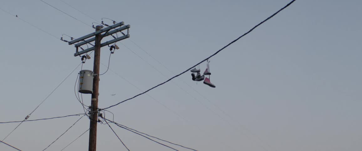 A pair of sneakers hangs from a power line next to a utility pole against a gray sky