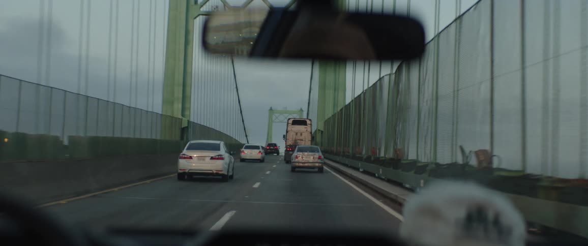A point-of-view shot from a car driving in traffic across a large suspension bridge on a cloudy day