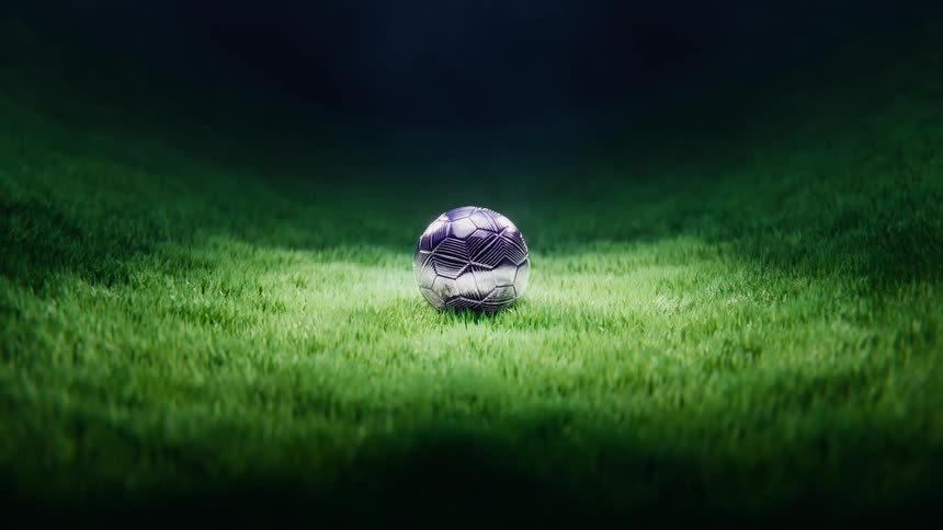 A futuristic metallic soccer ball lands in slow motion on a lush green field under a spotlight