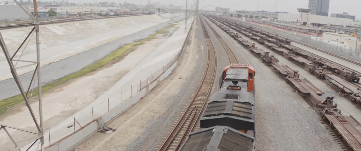 A freight train travels along the tracks in an industrial railyard on an overcast day