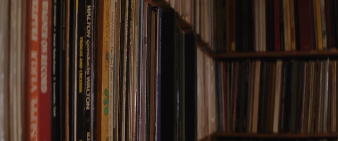 A slow-motion pan across a vast collection of classic vinyl records organized on a wooden bookshelf