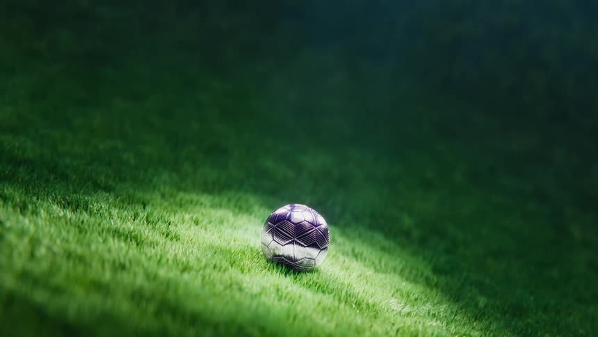 Dramatic slow zoom shot of a single soccer ball under a spotlight on a lush green grass field