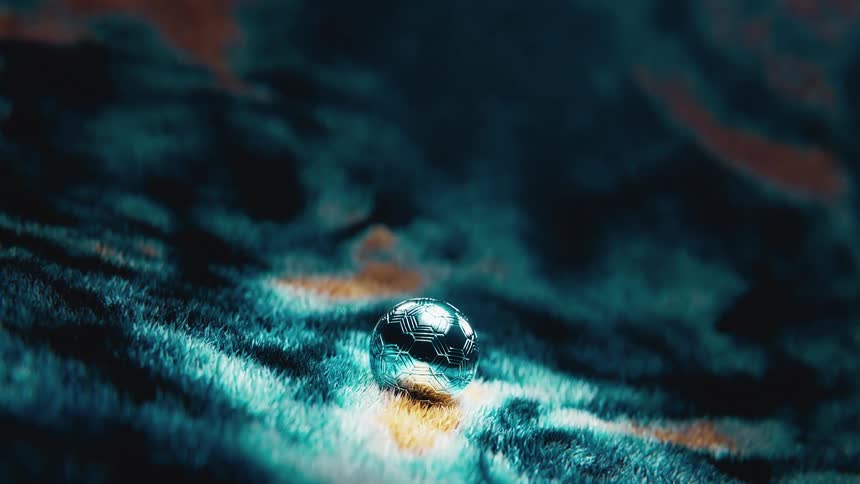 A mysterious, glowing metallic orb with intricate patterns sits on an otherworldly, furry surface as the camera slowly zooms in