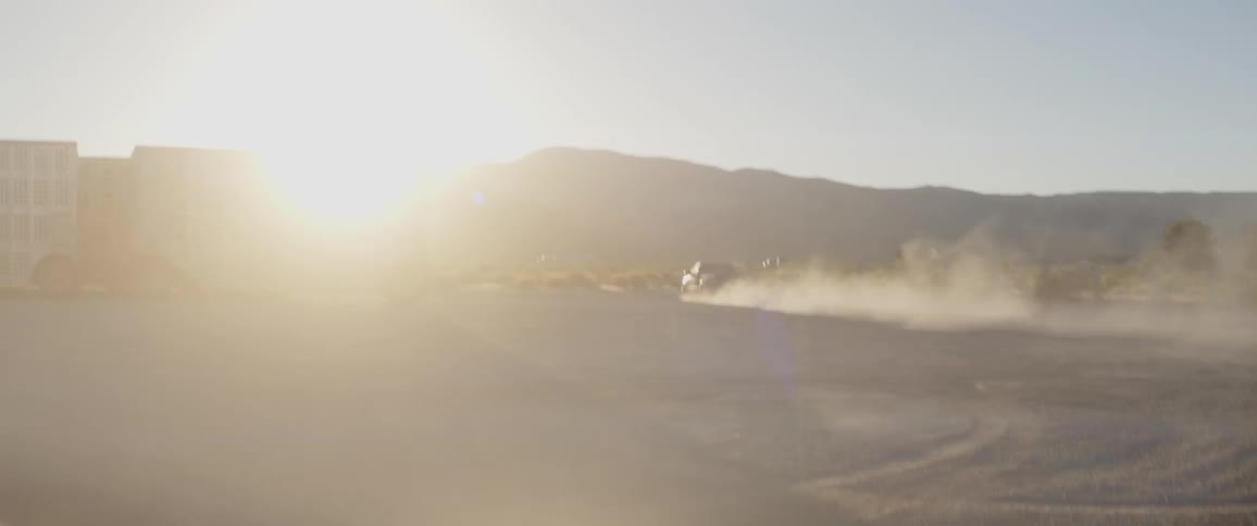 A black pickup truck kicks up a huge cloud of dust while doing a powerful burnout in the desert at sunset