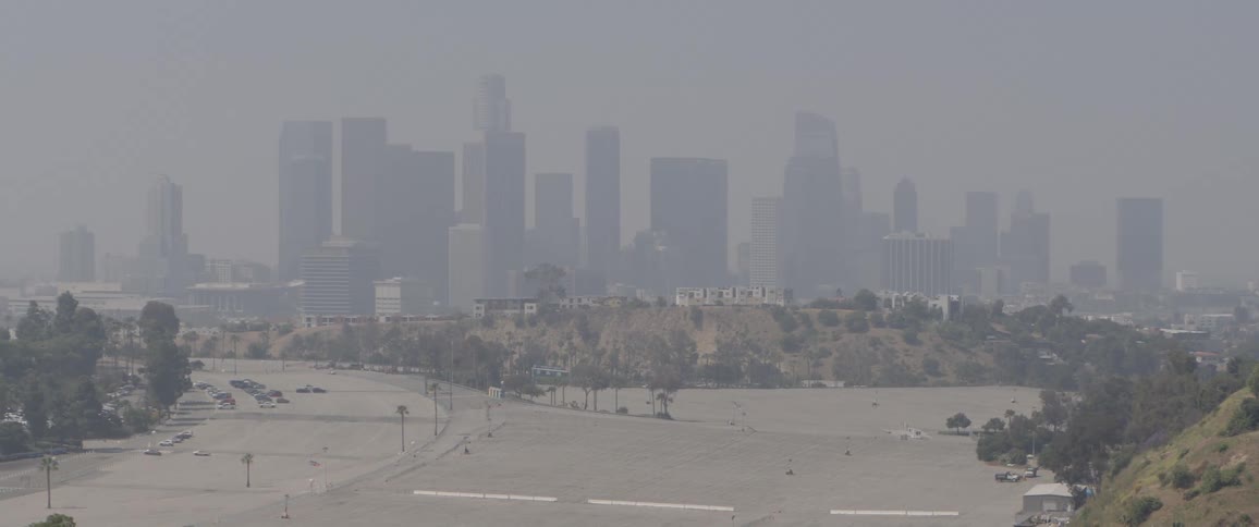 A static, wide shot shows the downtown Los Angeles skyline almost completely obscured by thick haze and air pollution