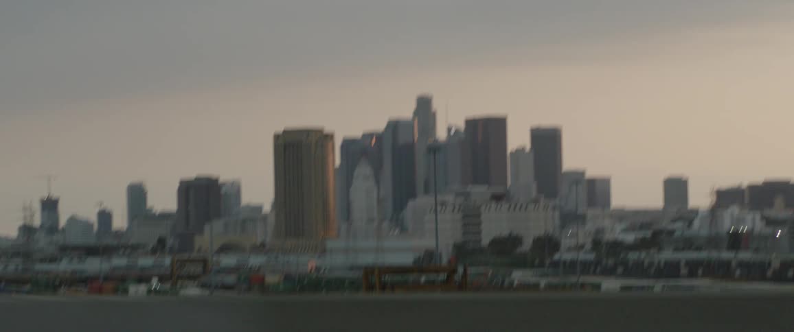 A passenger's point-of-view driving past the downtown Los Angeles skyline and a large industrial train yard at sunset
