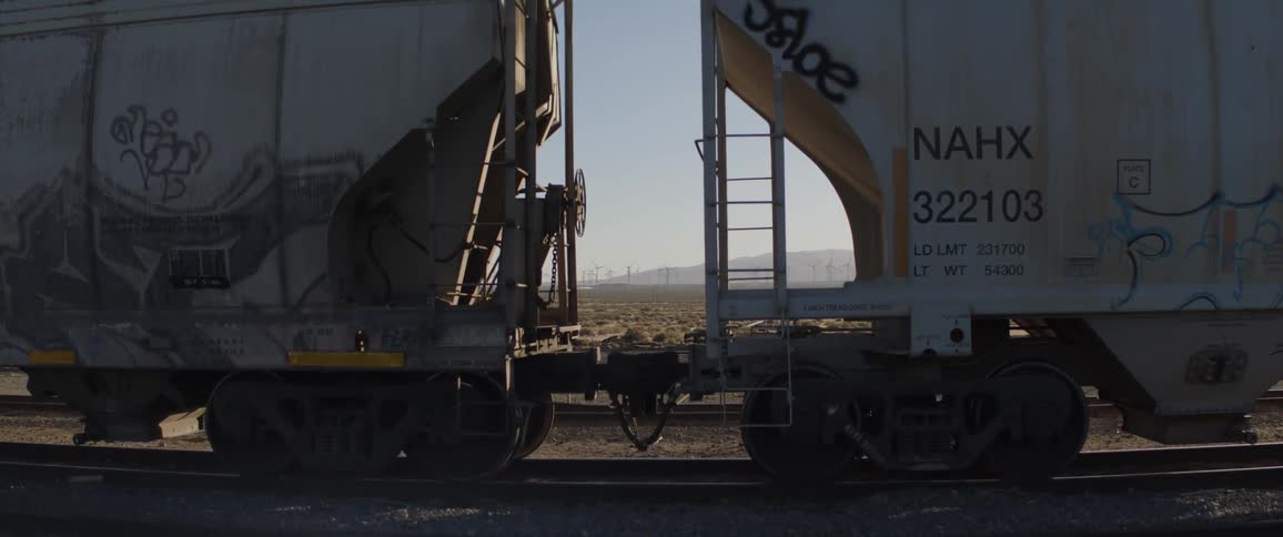 A view of a desert wind farm is framed perfectly between two stationary, graffiti-covered freight train cars