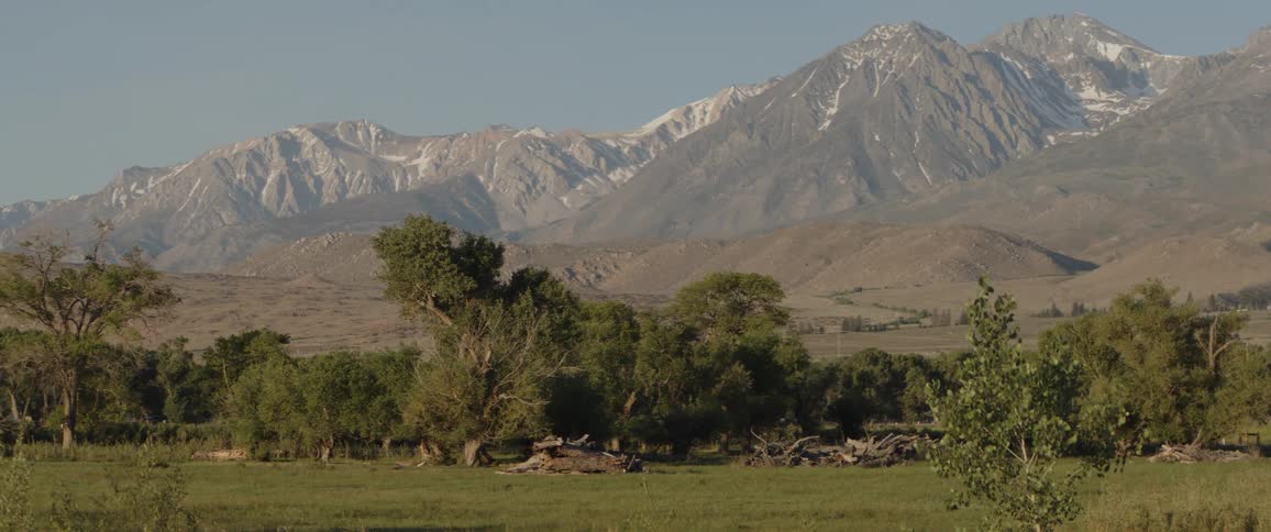 A slow pan reveals the snow-capped Sierra Nevada mountains rising above a lush green valley on a clear day