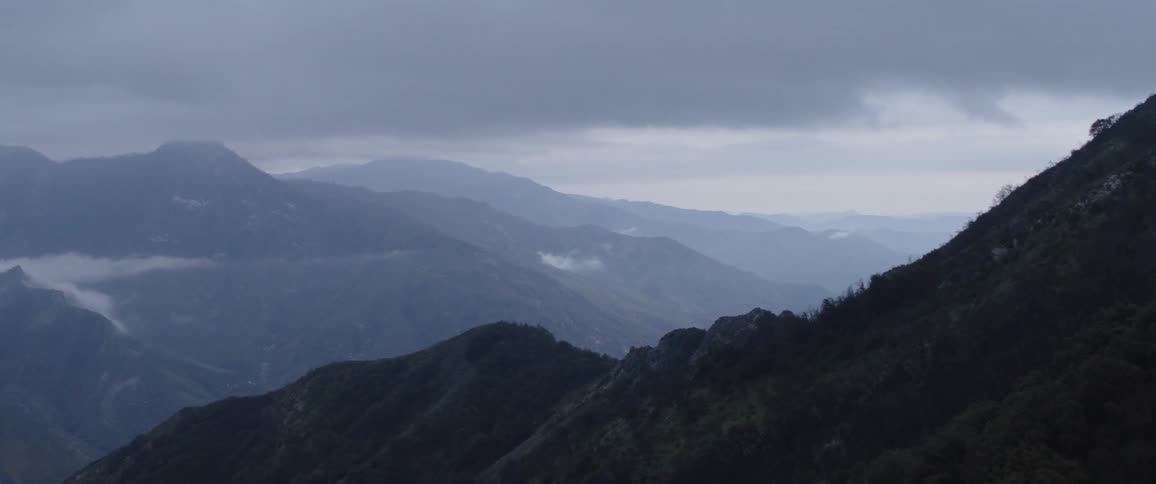 A panoramic view of a vast mountain range enveloped in fog on a gloomy, overcast day