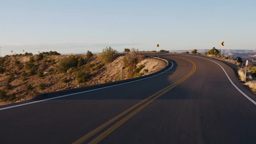 POV driving a winding mountain road through the desert landscape at sunset